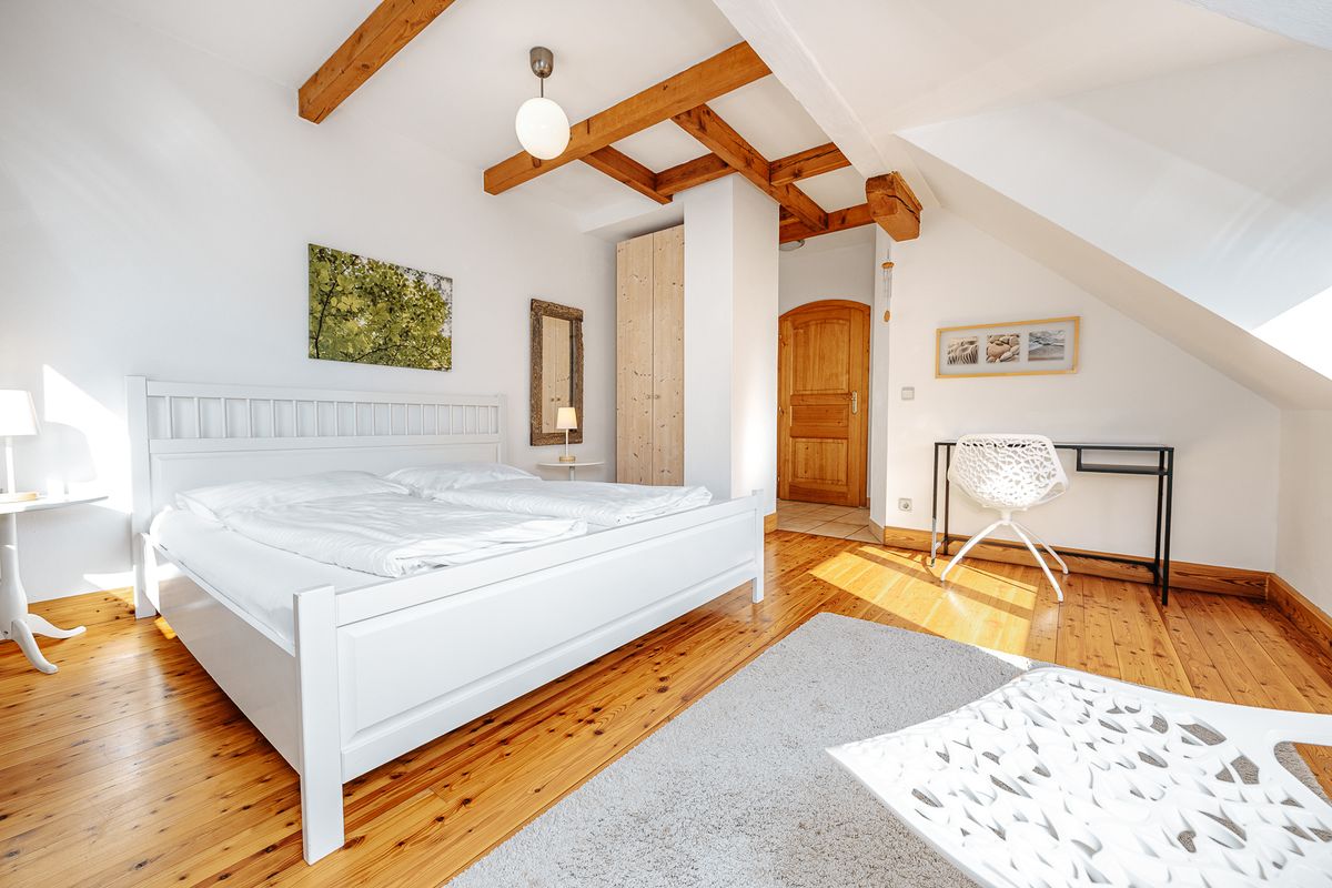Doppelzimmer mit weissem Bett, Holzbalken und Schreibtisch