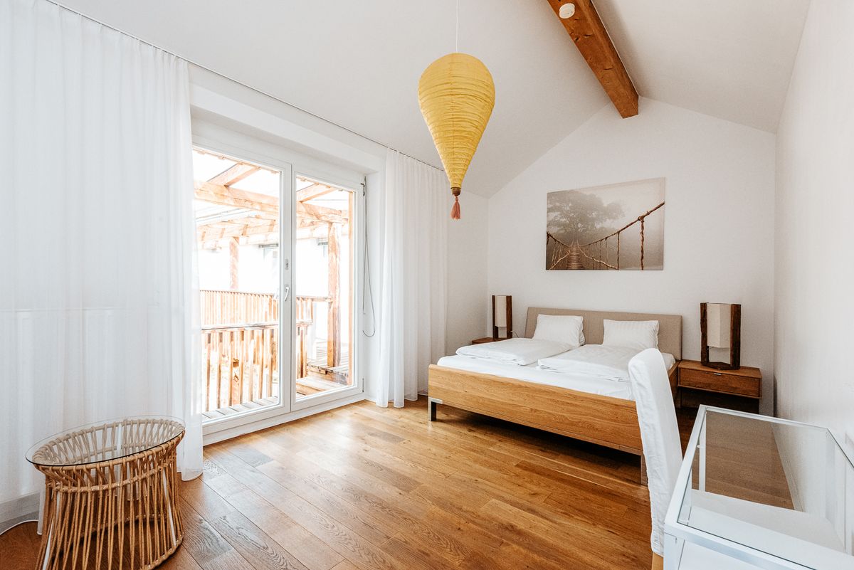Zimmer mit Balkontür, Holzbett und Blick auf die Pergola