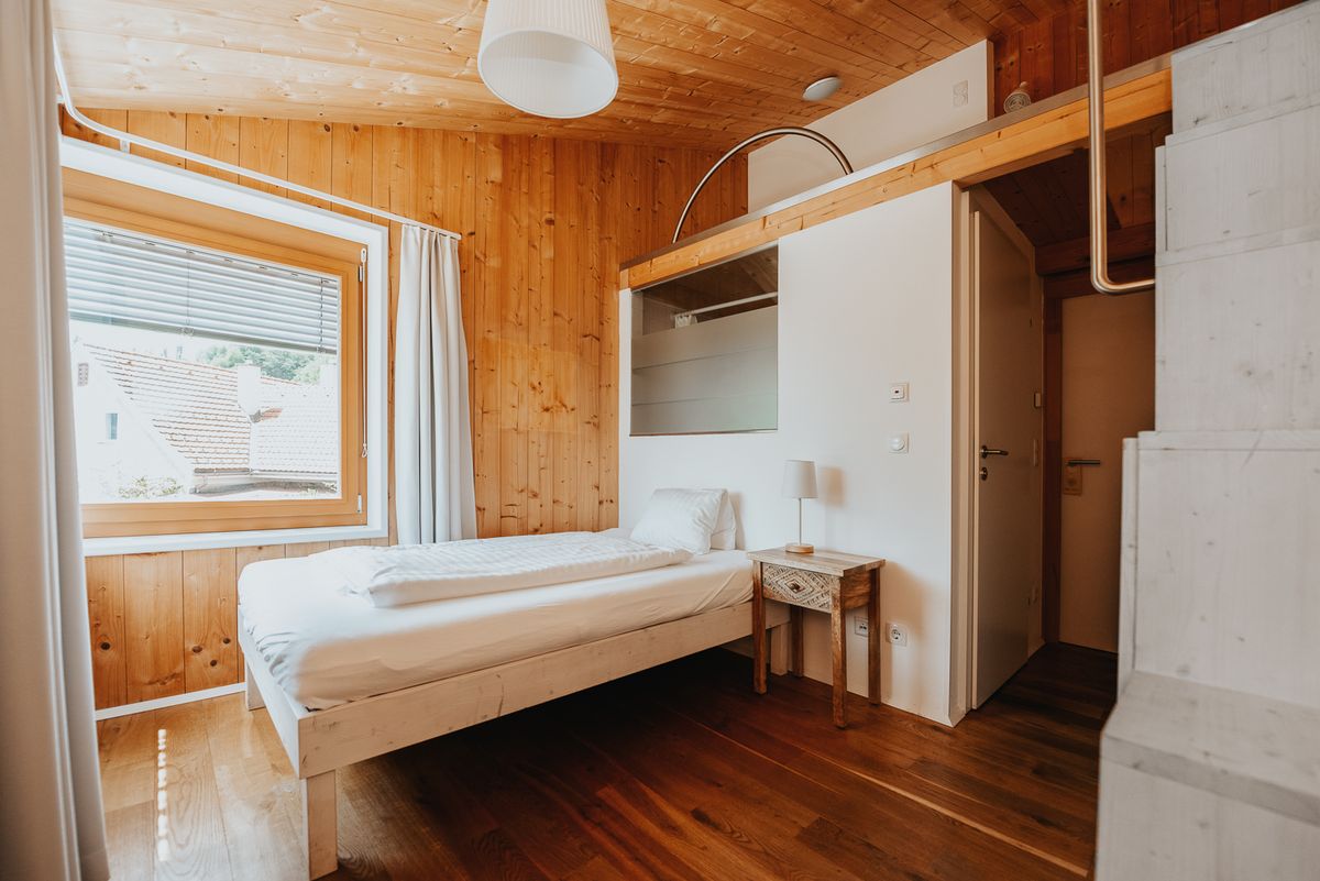 Klause mit Bett am Fenster, Holzwaenden und Blick ueber die Daecher